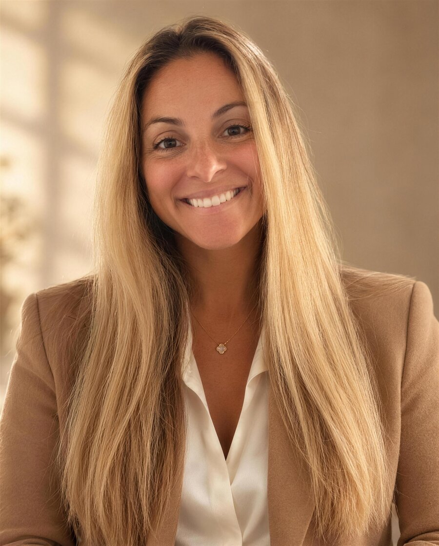 Retrato da Dra. Carminati sorrindo, de blazer caramelo e blusa branca